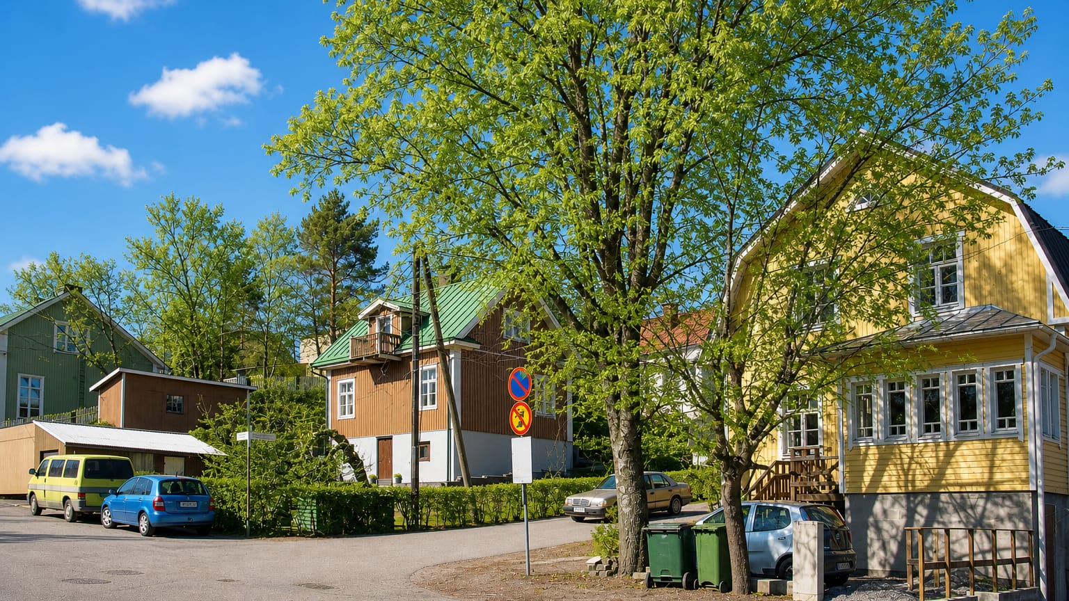 Street corner in Puistomäki, Turku, lined with yellow and brown wooden houses under fresh spring foliage.