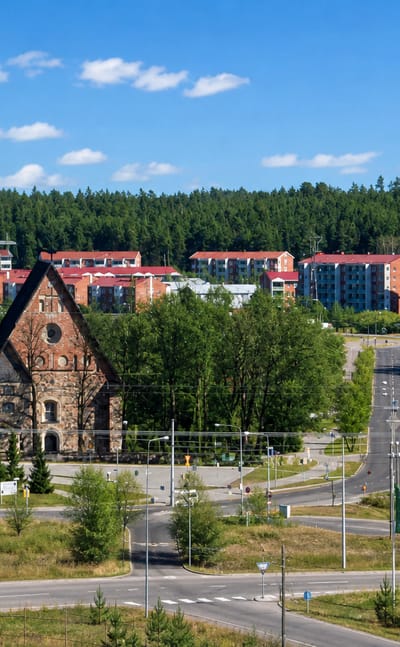 Greystone medieval church at Rantamaki in Turku, framed by red-brick apartment blocks and pine forest