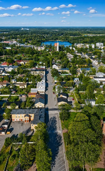 Aerial daytime view of Uusikaupunki, Finland, its red-brick neo-Gothic church and green spire amid leafy low-rise streets.
