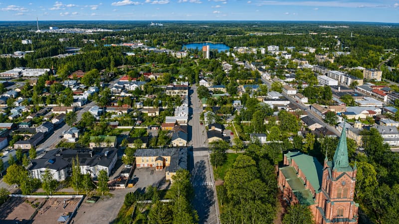 Aerial daytime view of Uusikaupunki, Finland, its red-brick neo-Gothic church and green spire amid leafy low-rise streets.