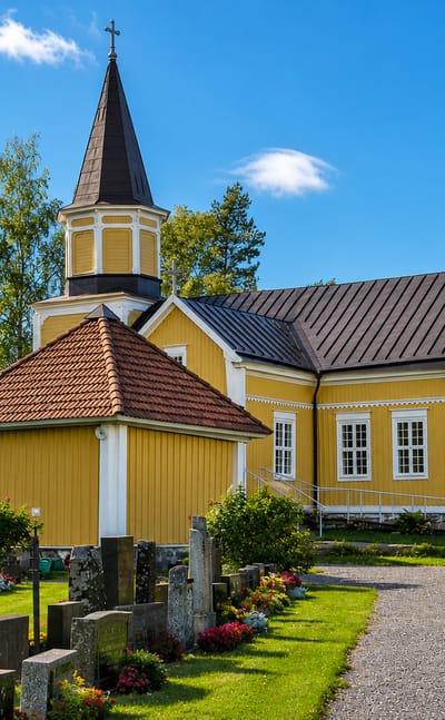 Yellow wooden church and its gravestone-filled churchyard under a blue sky in Vahto, Finland.