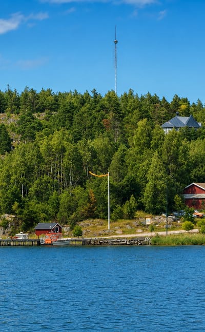 Boats moored by red waterfront cabins and a forested shore in the Västanfjärd archipelago, Finland