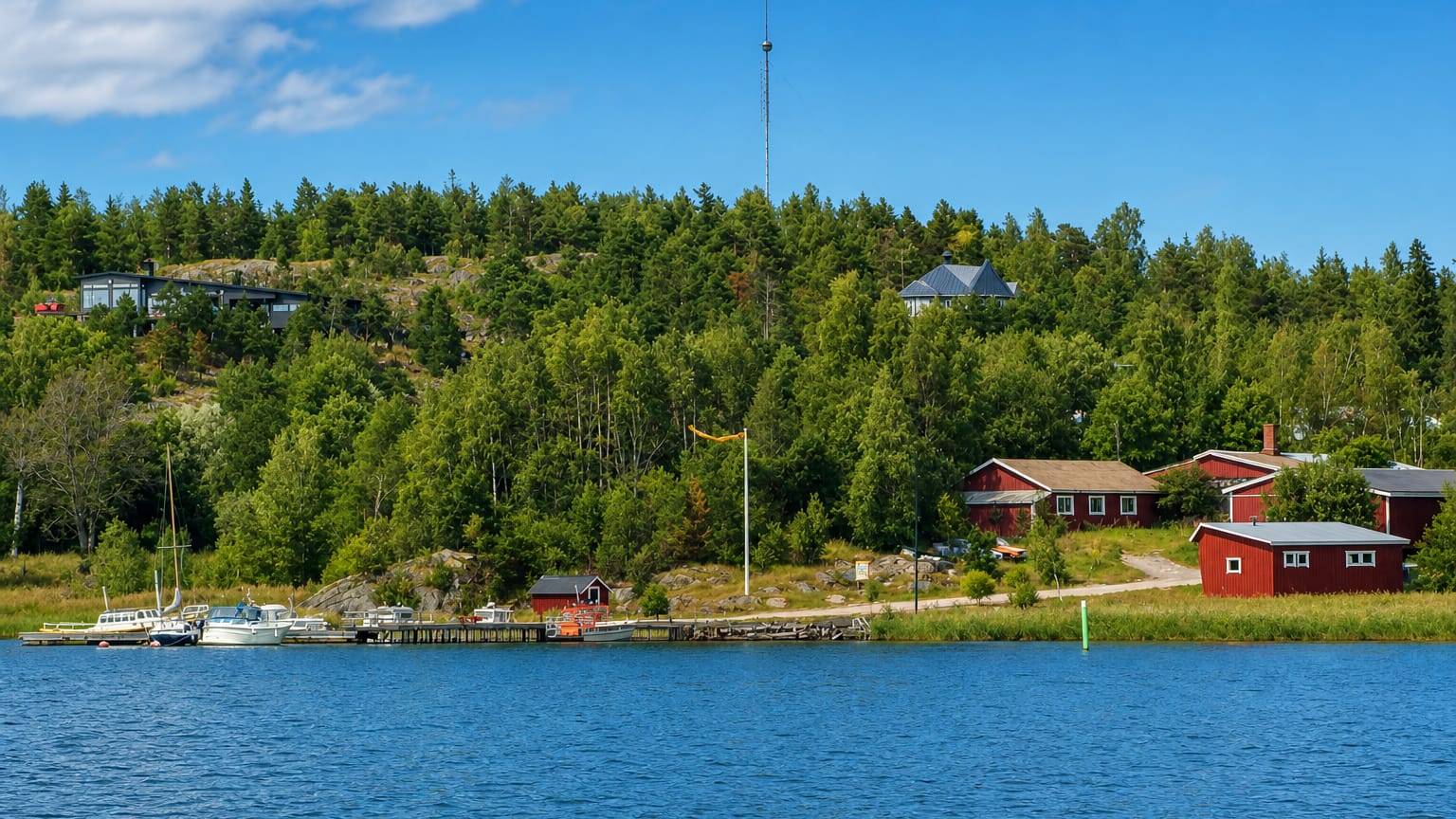 Boats moored by red waterfront cabins and a forested shore in the Västanfjärd archipelago, Finland