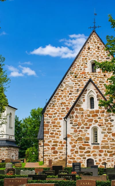 Medieval grey-stone church with a graveyard framed by trees at Vehmaa, Finland
