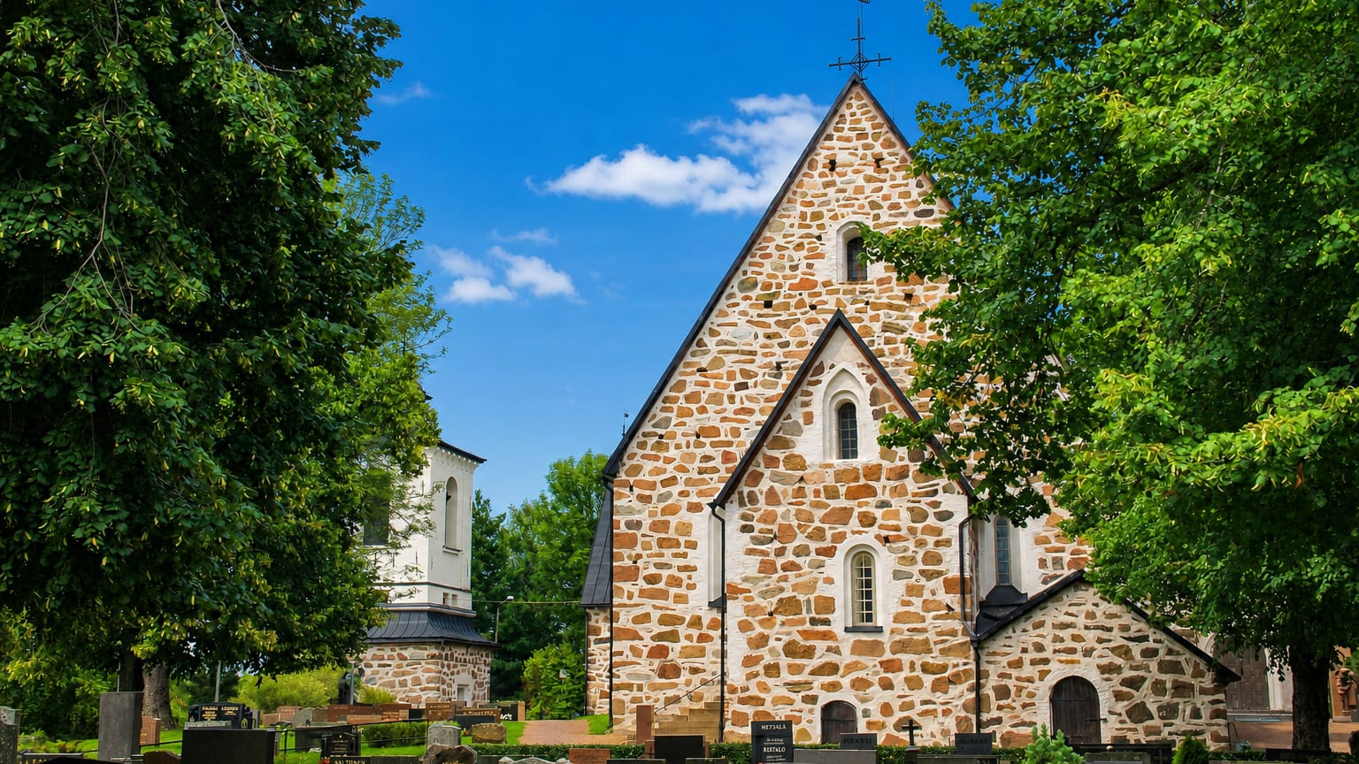 Medieval grey-stone church with a graveyard framed by trees at Vehmaa, Finland