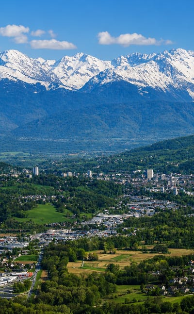 Chambery spread across a green valley beneath the snow-capped peaks of the Alps under blue sky
