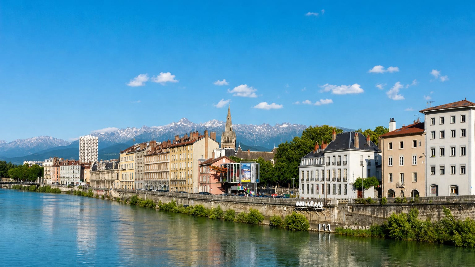 Grenoble quayside along the Isere with a church spire and snow-capped Alps rising behind the town.