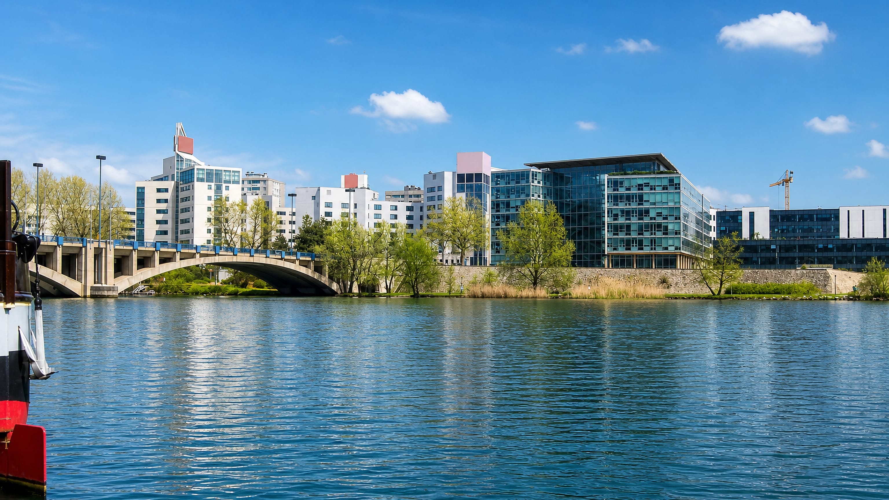 Riverside apartment blocks and glass offices in Gerland, Lyon, seen across the Rhône beside a road bridge.