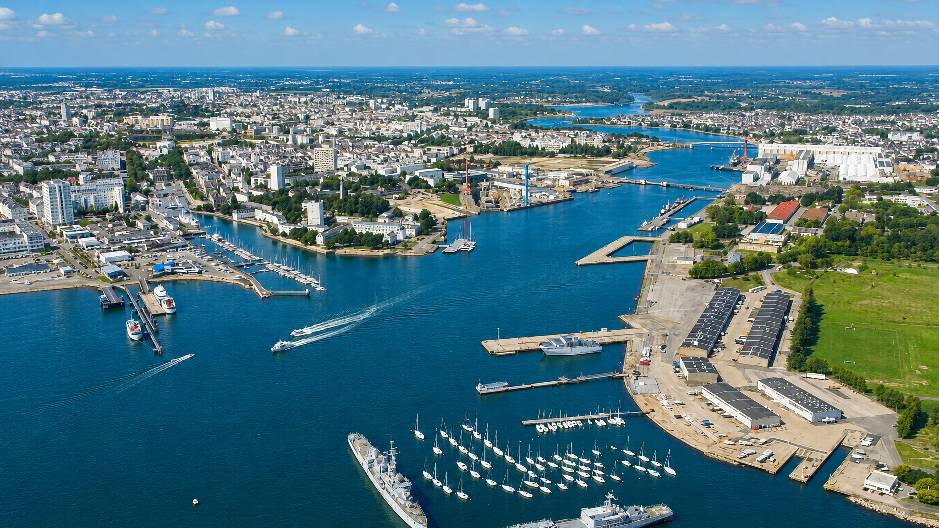 Aerial view over Lorient's harbour in Brittany, with naval vessels, a yacht marina and the estuary beyond.