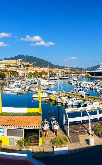 Ajaccio's boat-filled marina and pastel waterfront with a cruise ship and Corsican mountains behind.