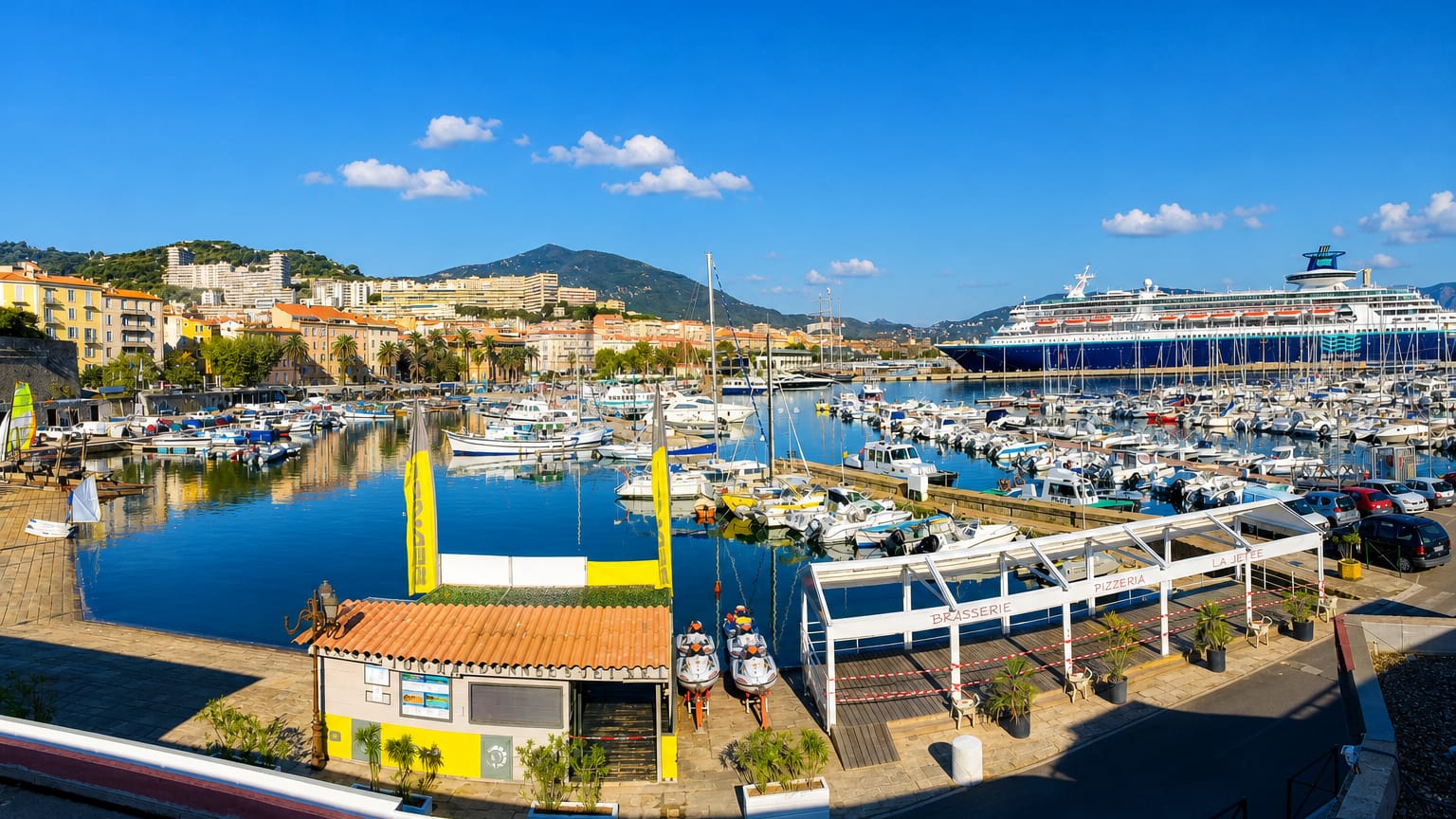 Ajaccio's boat-filled marina and pastel waterfront with a cruise ship and Corsican mountains behind.