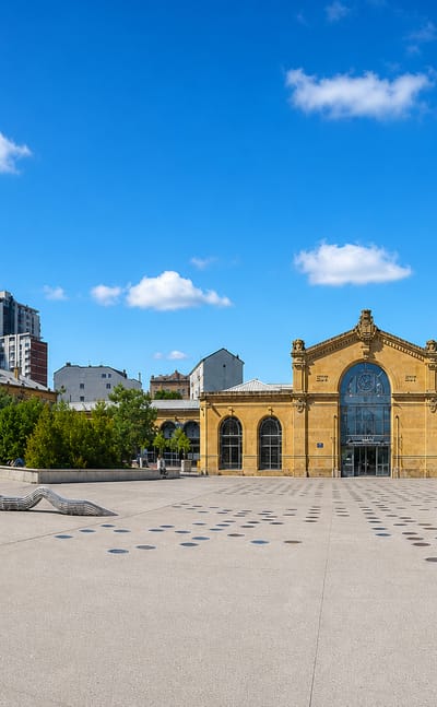 A wide paved public square in Nancy fronting an ornate 19th-century yellow-stone market pavilion