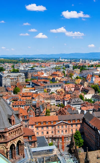 Strasbourg's old-town red rooftops and sandstone church spires viewed from above under blue sky.