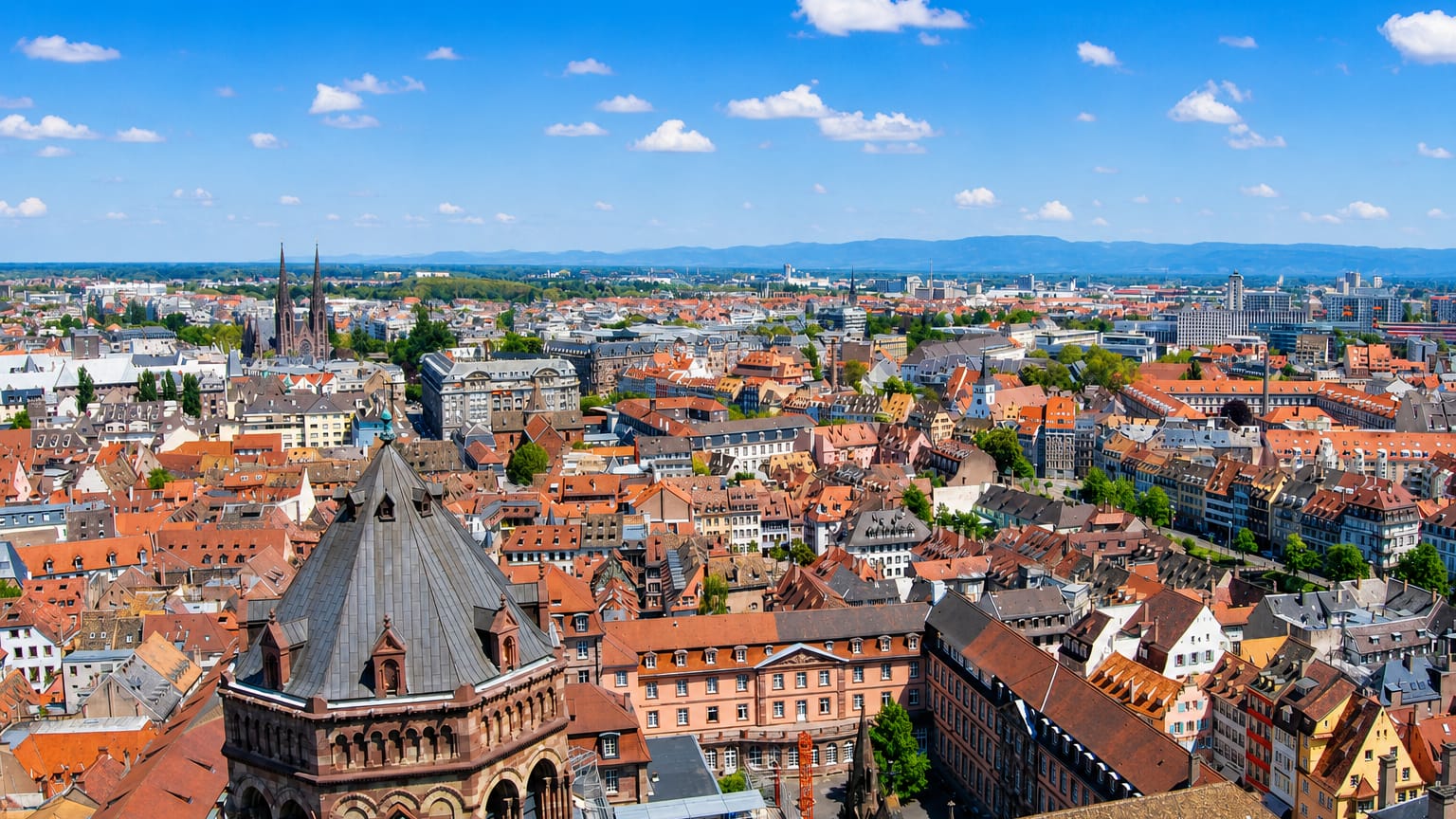 Strasbourg's old-town red rooftops and sandstone church spires viewed from above under blue sky.