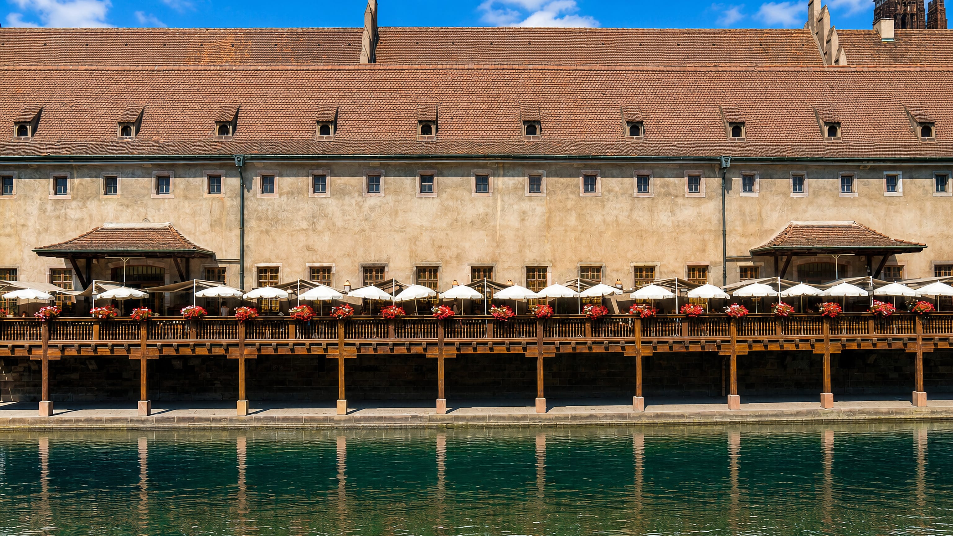 A long tiled-roof building with a riverside restaurant terrace on the Ill in Krutenau, Strasbourg.