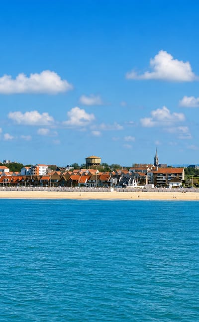 Calais seafront across the Channel, sandy beach backed by apartment blocks, a belfry spire and water tower.