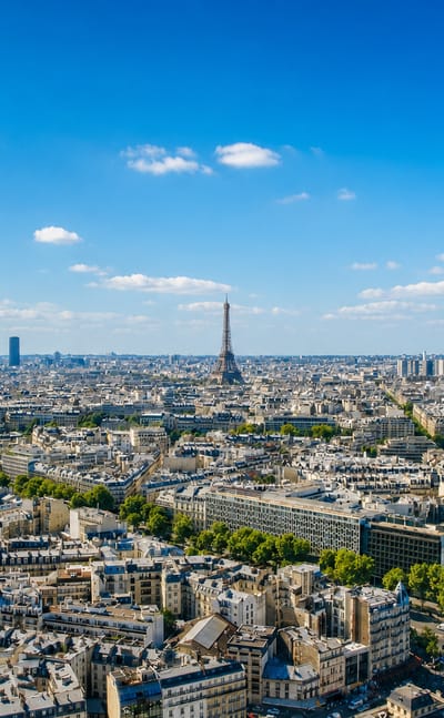 Paris skyline with the Eiffel Tower and Montparnasse Tower rising over Haussmannian rooftops under a bright sky.