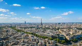 Paris skyline with the Eiffel Tower and Montparnasse Tower rising over Haussmannian rooftops under a bright sky.