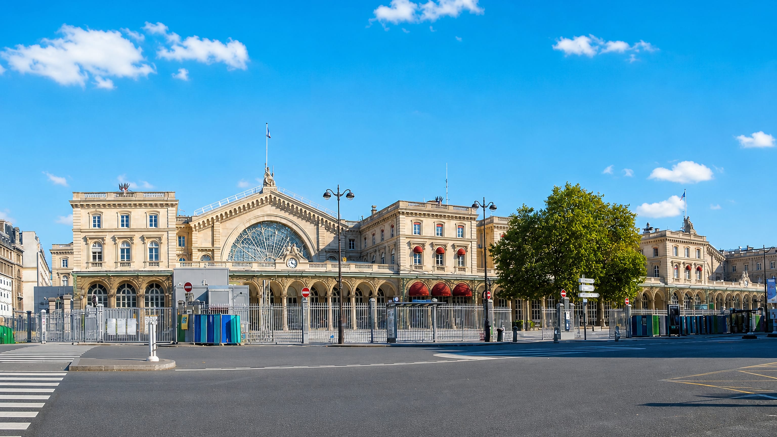 The stone facade and arched glass hall of Gare de l'Est in the 10th arrondissement of Paris under blue sky.