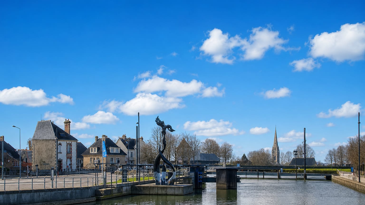 A canal lock and modern sculpture at Caen with stone Normandy houses and a distant church spire