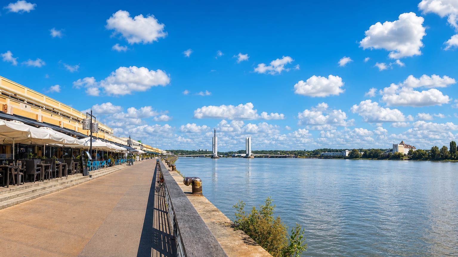 Bordeaux Garonne riverfront quay with waterside terraces and the Chaban-Delmas lift bridge in the distance.