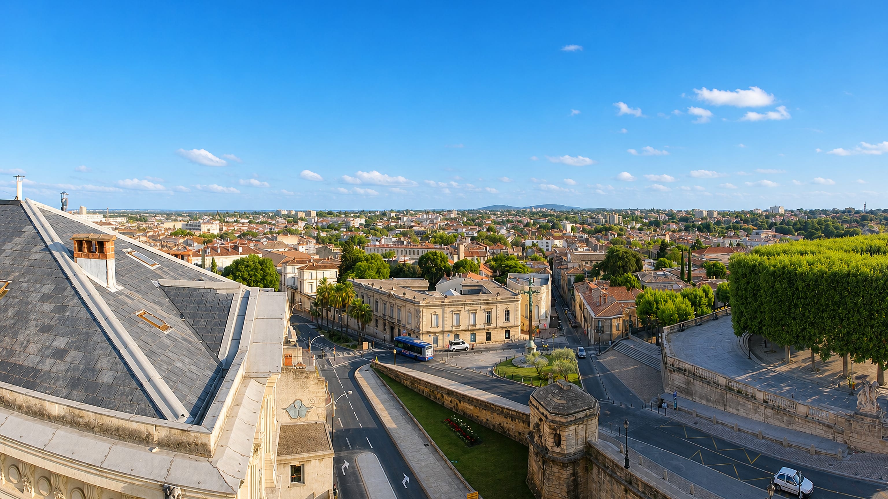 Elevated view over Montpellier's terracotta rooftops, tree-lined promenade and classical buildings.