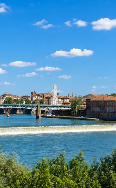 Toulouse's Garonne riverfront with its weir, arched bridge and the green dome of La Grave amid pink-brick buildings.