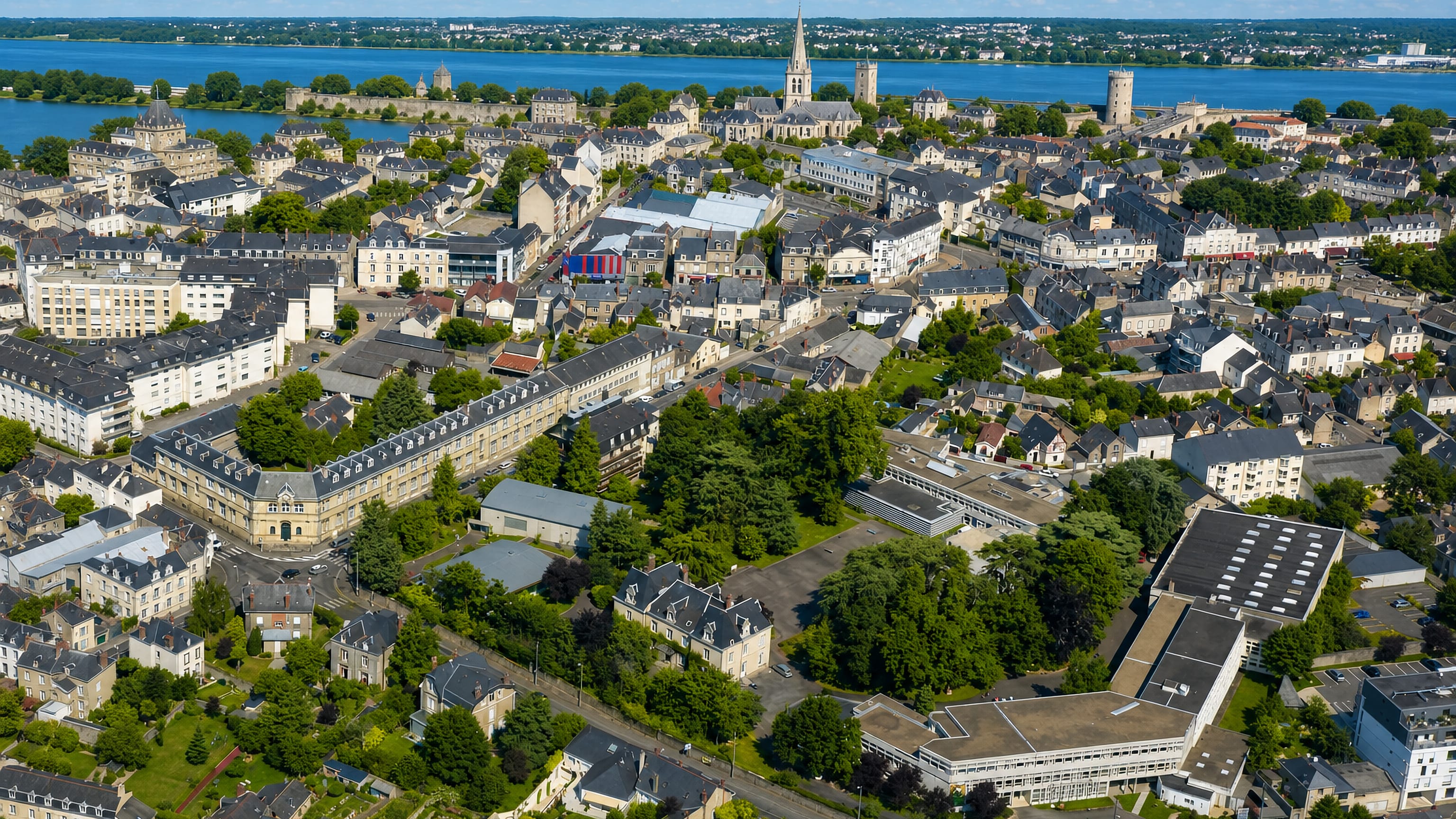 Aerial view over Laval's slate rooftops, church spire and castle keep beside a broad stretch of the Mayenne.