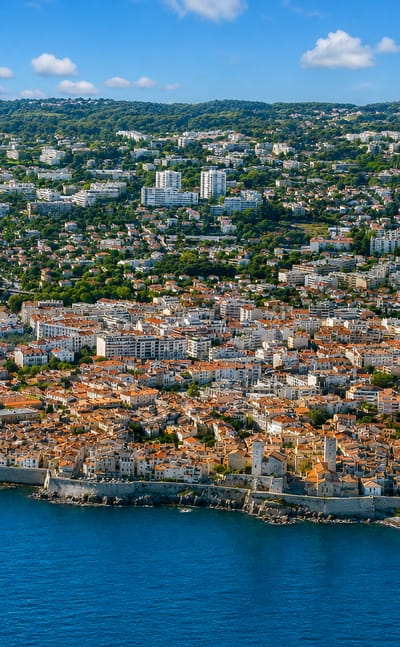 Aerial view of Antibes' walled old town and terracotta rooftops on a Mediterranean promontory beside its marina.