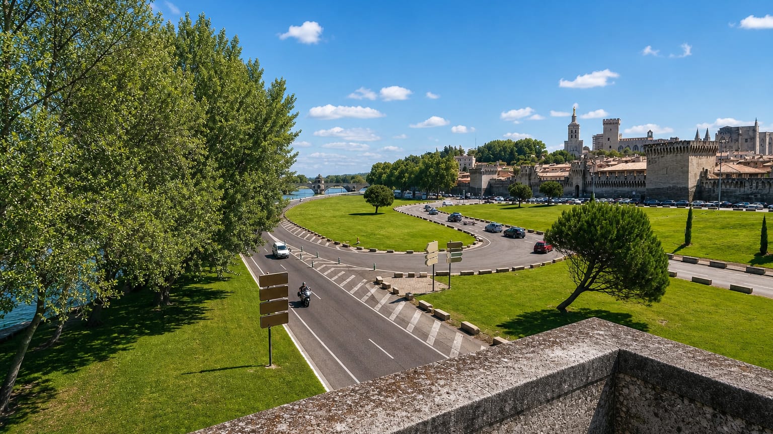 Avignon's Palais des Papes and ramparts rising above the Rhone with a tree-lined riverside park.
