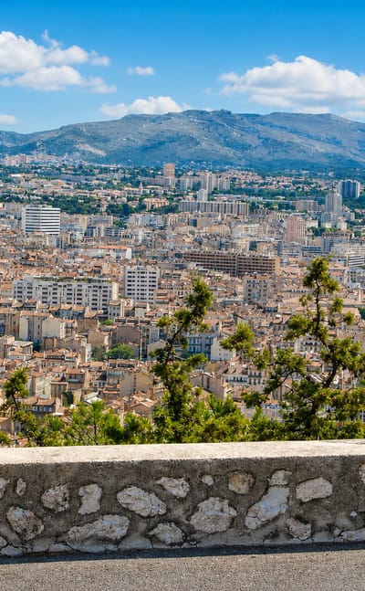 Elevated view over Marseille's terracotta rooftops and dense townscape backed by the surrounding limestone hills.