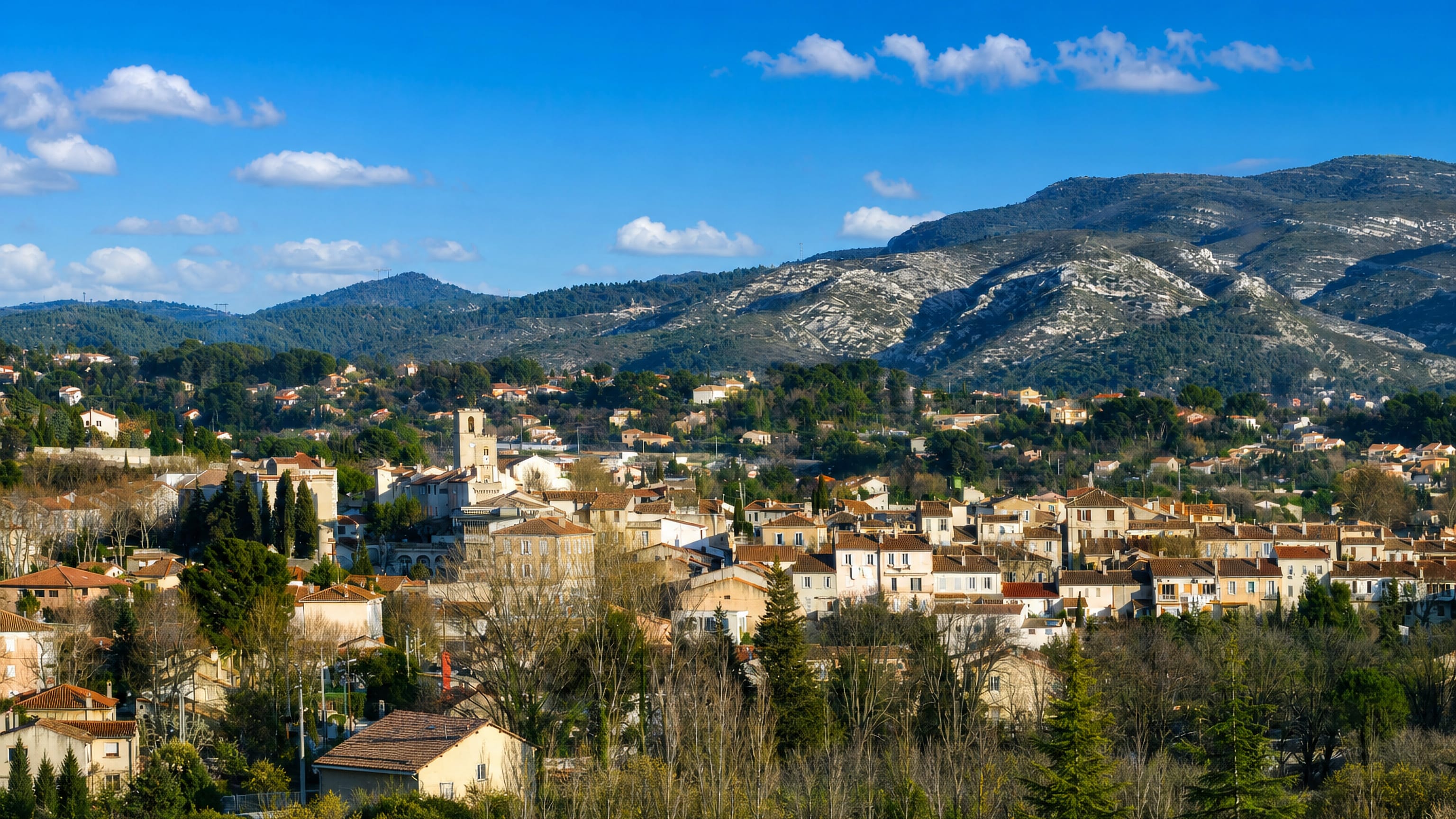 Tiled roofs and a church bell tower below limestone hills at Château Gombert, northern Marseille.