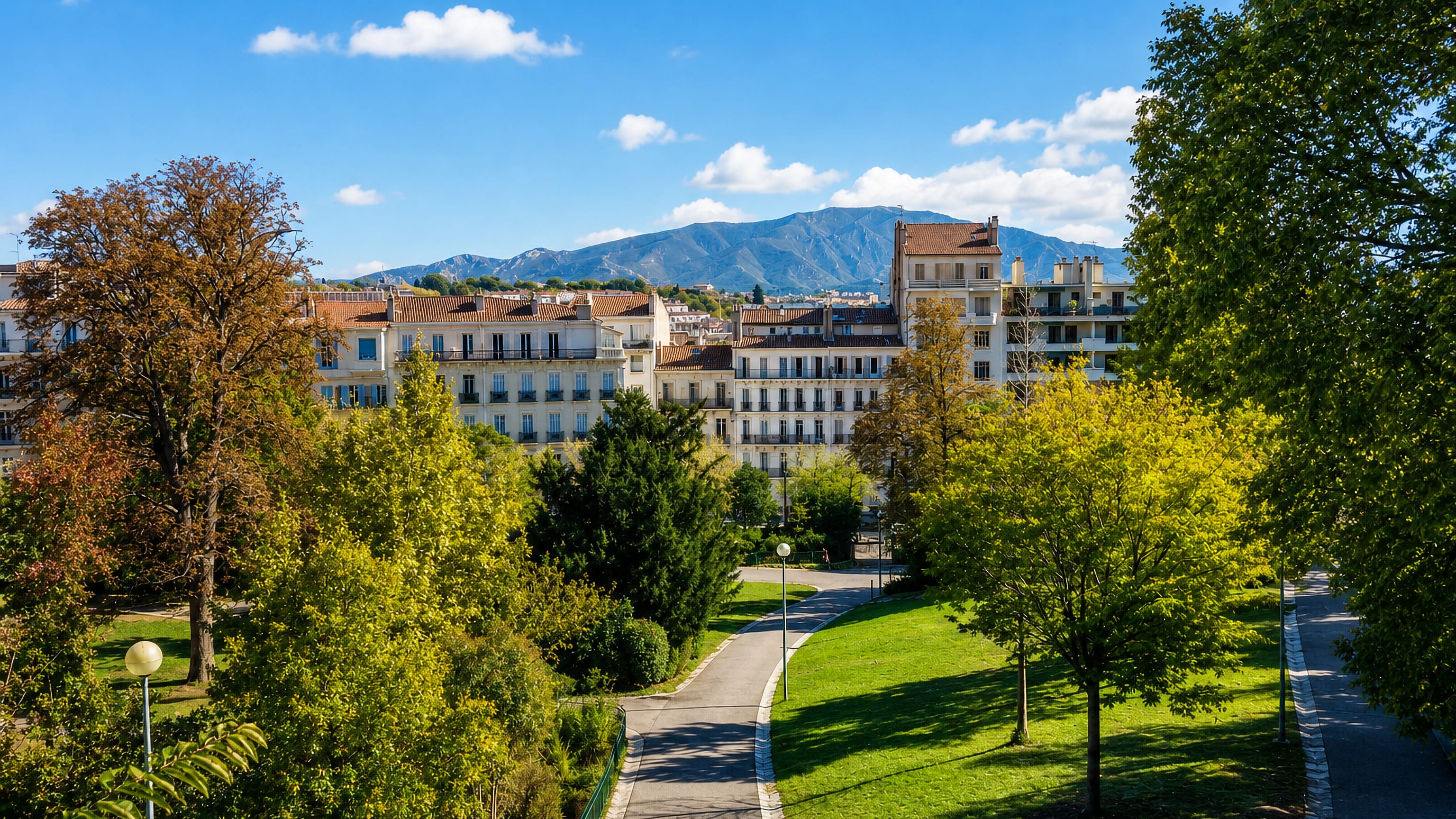 Park lawns and paths below Haussmann-style facades in Cinq Avenues, Marseille, with limestone hills behind.