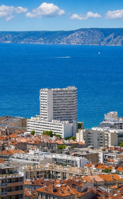 Marseille rooftops above the blue Mediterranean bay near Le Pharo, with the coastal hills beyond.