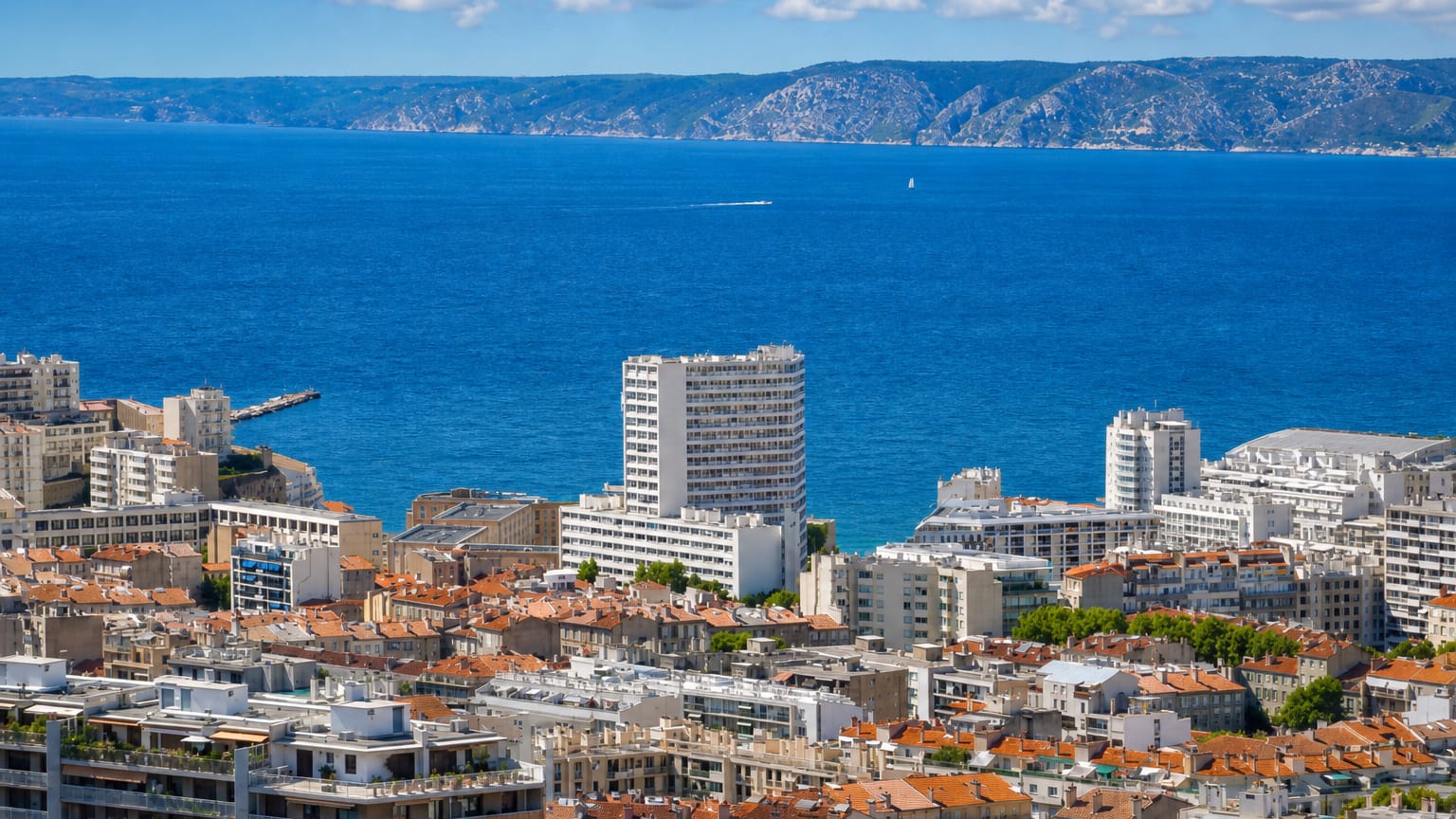 Marseille rooftops above the blue Mediterranean bay near Le Pharo, with the coastal hills beyond.