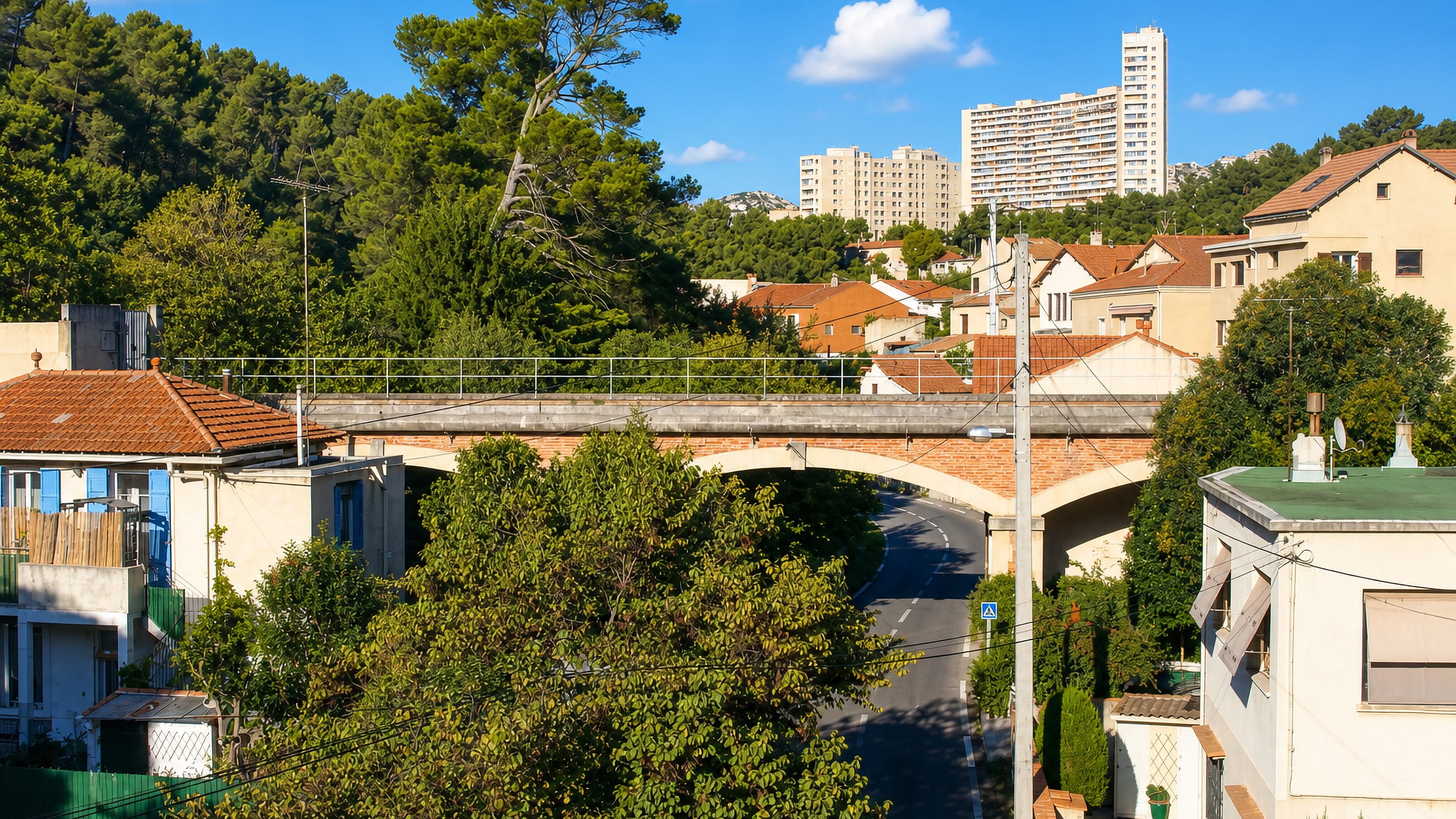 Stone road bridge, pines and tiled roofs below hilltop apartment towers in Le Redon, Marseille.