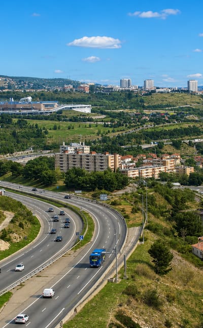 A motorway curving through hills past apartment blocks toward the distant Marseille skyline at Saint-Henri.
