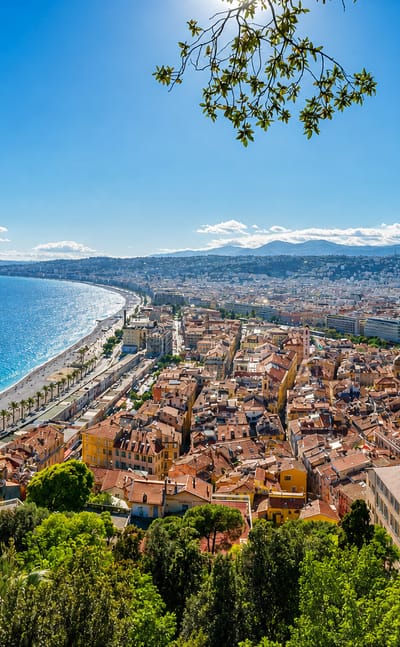 Elevated view over Nice's Baie des Anges, the pebble beach, Promenade des Anglais and terracotta-roofed Old Town beside the blue Mediterranean.