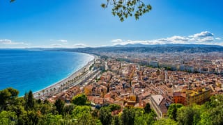 Elevated view over Nice's Baie des Anges, the pebble beach, Promenade des Anglais and terracotta-roofed Old Town beside the blue Mediterranean.