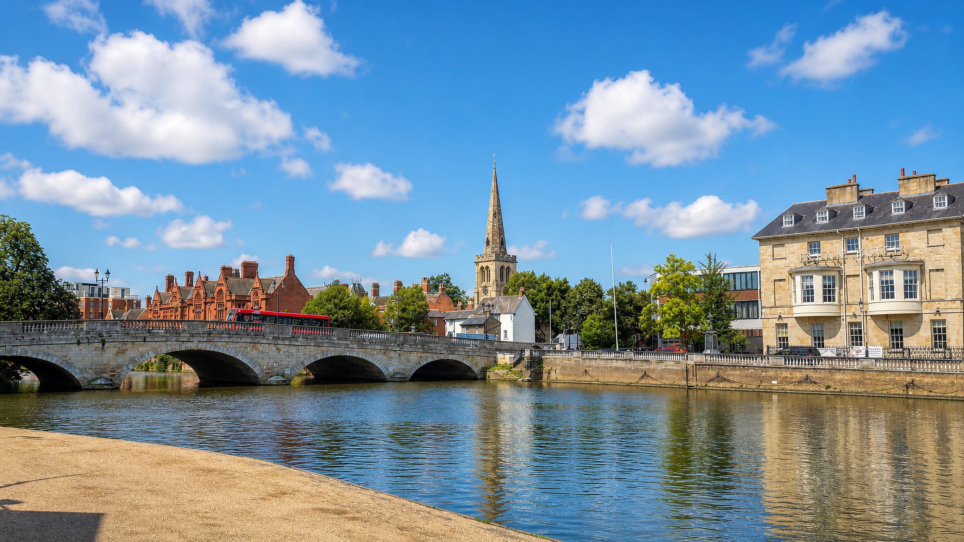 Bedford's stone Town Bridge over the River Great Ouse, with a red bus crossing and a church spire above the town.