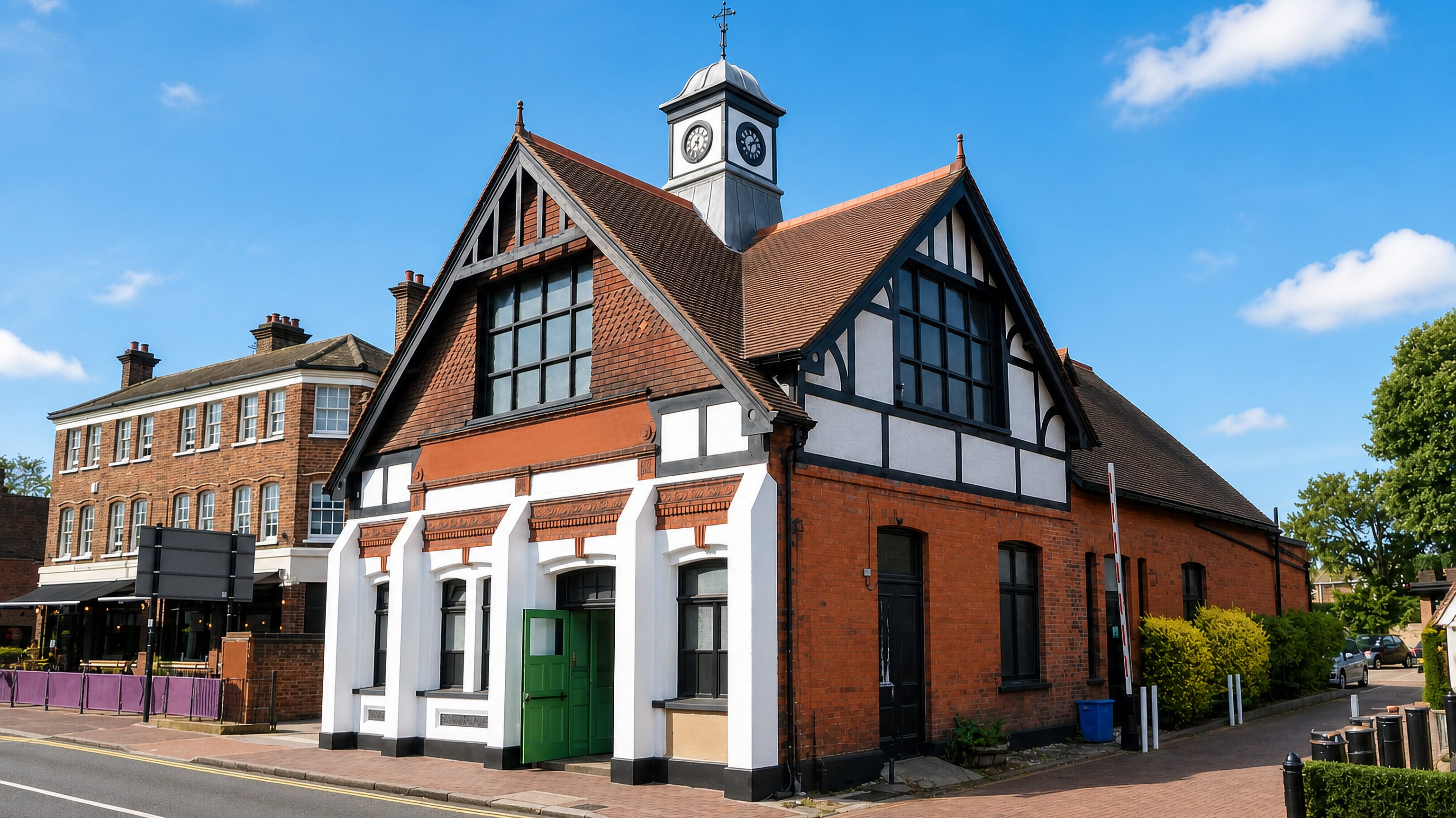 Red-brick Tudor-style hall with a clock turret on a sunlit street corner in Bexley, London.