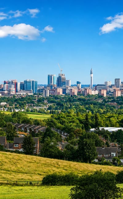 Birmingham, England skyline with the BT Tower and clustered high-rises viewed across green fields and suburbs.