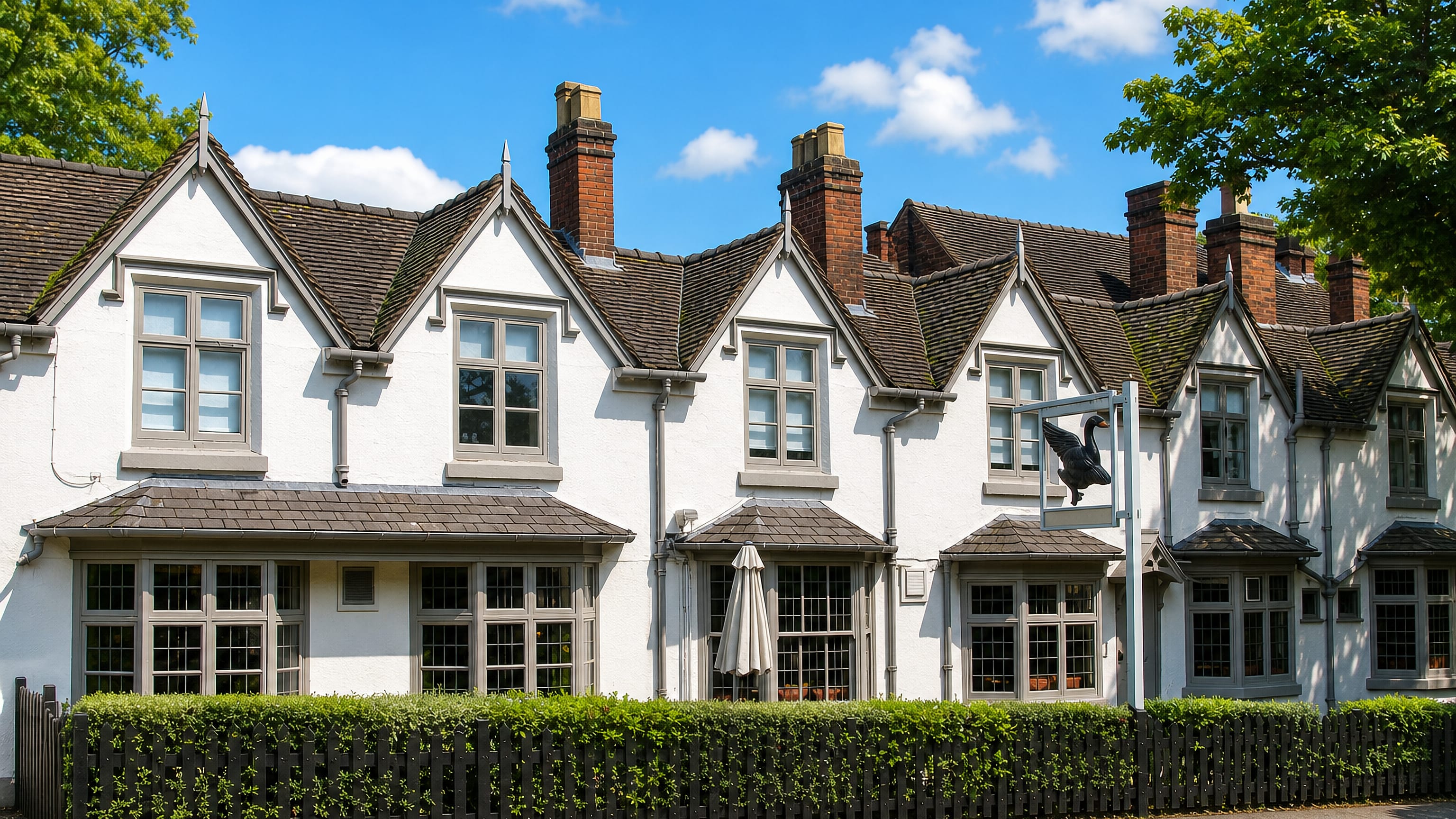White gabled Victorian terrace with brick chimneys and a hanging pub sign on Harborne's high street, Birmingham.