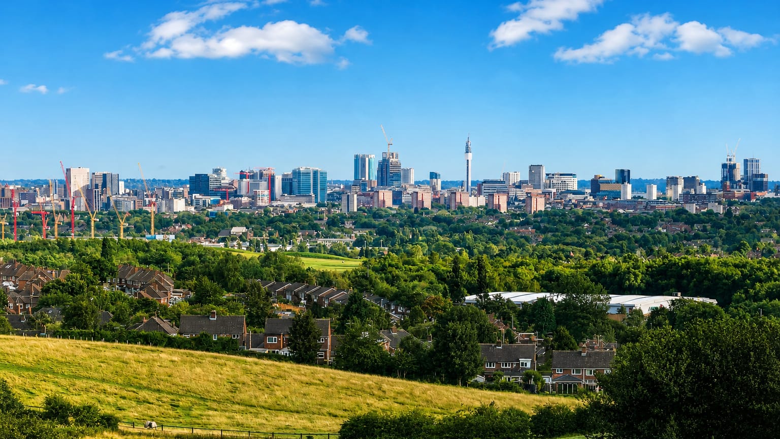 Birmingham, England skyline with the BT Tower and clustered high-rises viewed across green fields and suburbs.