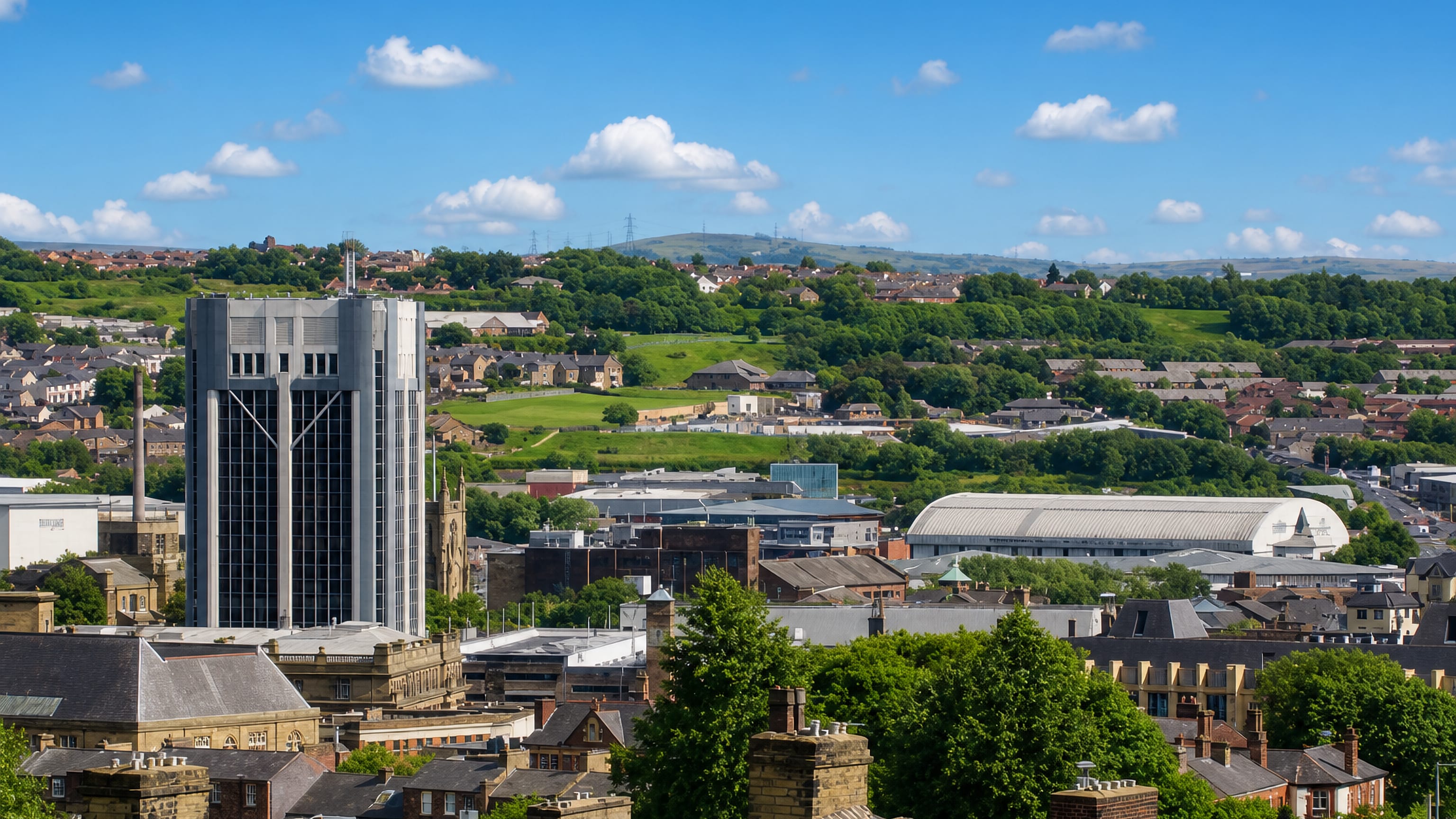 Blackburn's slate rooftops and modernist office tower with the green Lancashire hills rising beyond the town centre