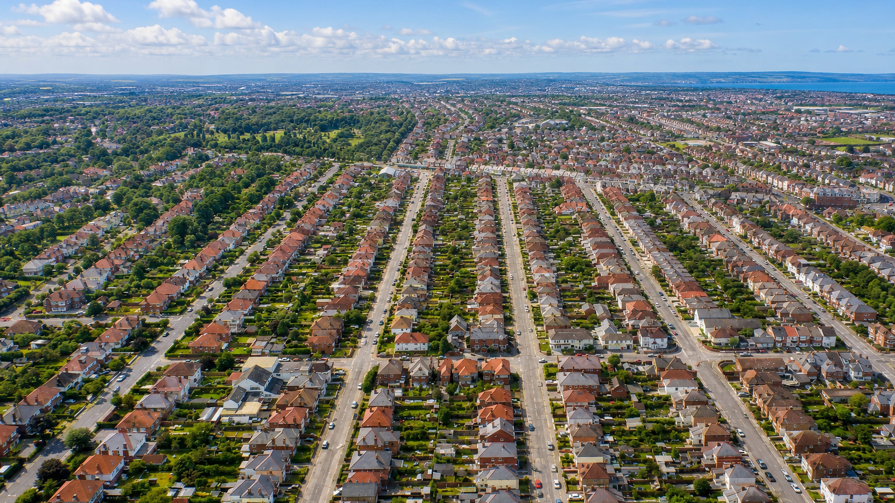 Aerial view over the terraced streets and gardens of Charminster in Bournemouth with the sea beyond.