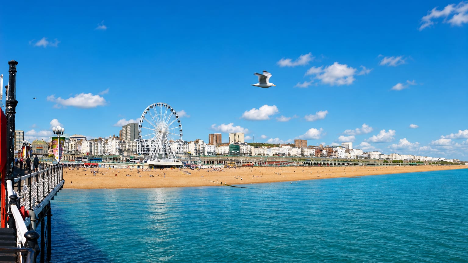 Brighton seafront with the beach, promenade, and a large observation wheel seen from the pier.