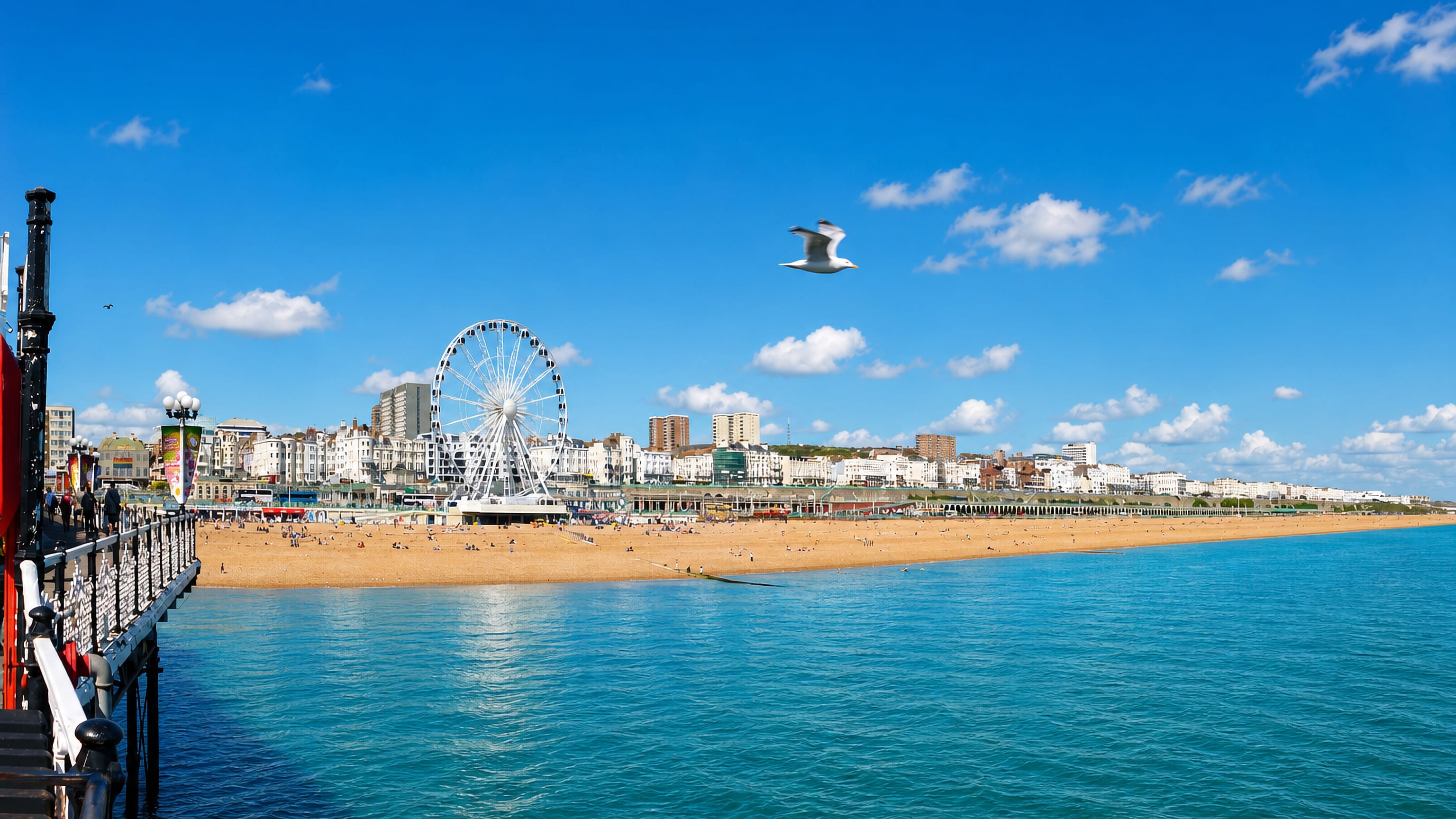 Brighton seafront with the beach, promenade, and a large observation wheel seen from the pier.