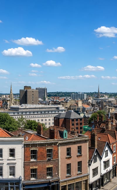Bristol rooftops with colourful Georgian terraces, church spires and the Wills Memorial Tower under blue sky.