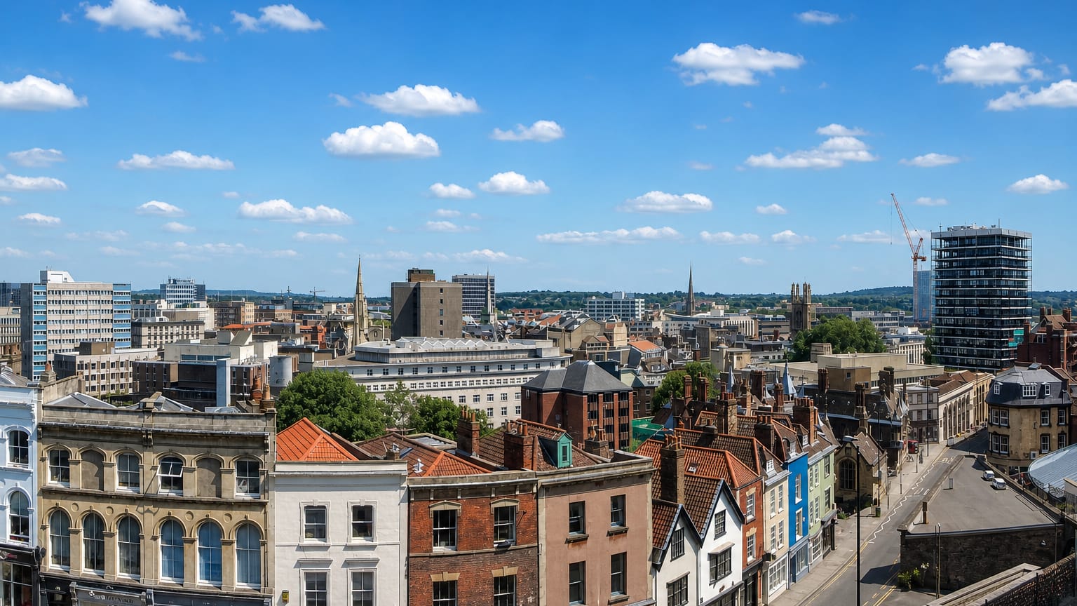 Bristol rooftops with colourful Georgian terraces, church spires and the Wills Memorial Tower under blue sky.